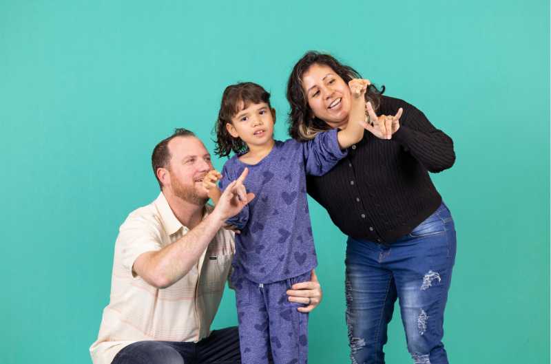 Mom and dad helping little girl learn to sign