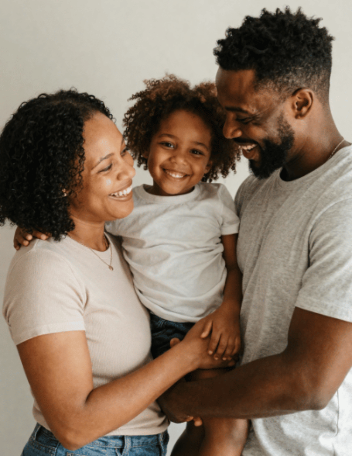 Adult caregivers holding a young child together and posing for a family portrait.