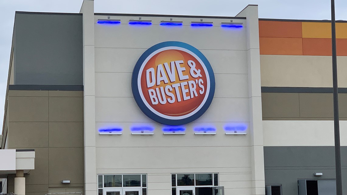 Exterior of a Dave & Buster's entertainment venue featuring the large circular Dave & Buster's logo mounted on the front of the building above the main entrance.